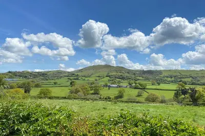 a green field with hills and clouds in the sky at Camlad Barn in Chirbury