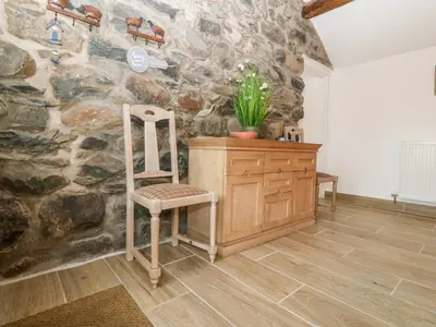 a stone wall with a chair and a wooden cabinet at Y Bwthyn in Dyffryn