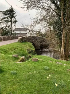 a stone bridge over a river in a field at Cosy Arts & Crafts Cottage with stunning views in Brecon