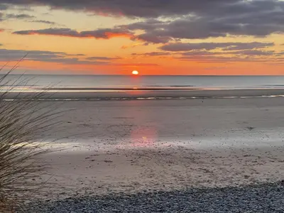 a sunset on the beach with the sun in the distance at Beautiful Aberdovey Seafront Apartment 2 in Aberdyfi