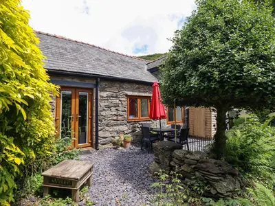 a stone cottage with a table and a red umbrella at Hen Bopty in Fairbourne