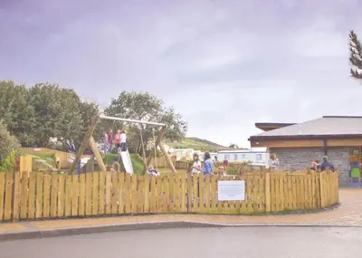 a group of people playing on a playground behind a wooden fence at Sunbeach Holiday Park in Llwyngwril