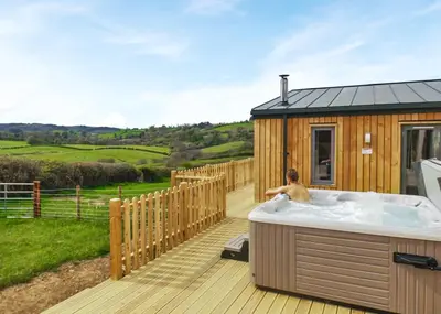 a man in a hot tub on a deck at Castle Pren Lodges in Llanddewi Ystradenny