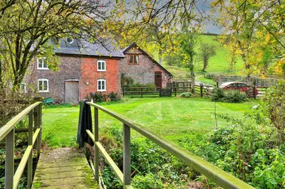 a wooden bridge leading to a house with a yard at Finest Retreats - Great Cantal Granary in Llandrindod Wells