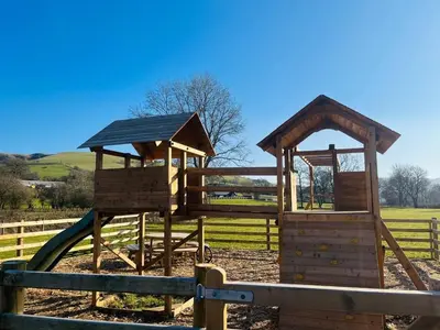 a wooden playground with a slide in a fence at Hillside Lodge in Nantmel