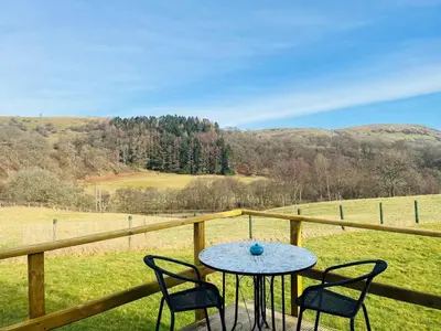 a table and chairs on a porch with a view of a field at Hwyl in Abbey-Cwmhir