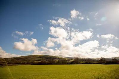 a large green field with a blue sky and clouds at Pentre Fach in Llanddewi Ystradenny