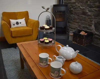 a coffee table with tea cups and cupcakes on it at Yr Hen Beudy in Aberystwyth