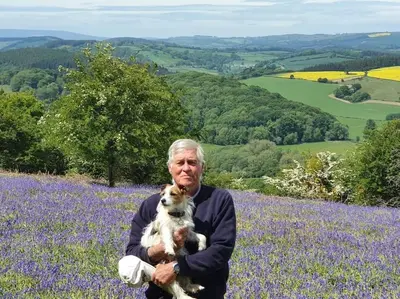 an older man holding a dog in a field of flowers at Delightful Country Cottage in a lovely rural area in Ludlow