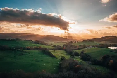 a sunset over a green field with the sun shining at Bedw Barn in Newtown