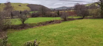 a green field with trees and mountains in the background at The Stables in Tregaron