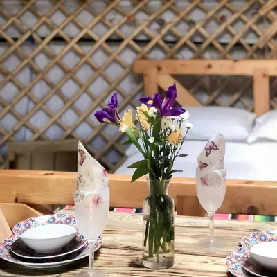 a table with a vase of flowers and two glasses at 'Villager' the Yurt at Pentref Luxury Camping in Penuwch