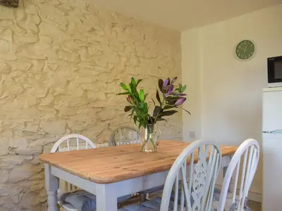 a dining room table with white chairs and a vase with flowers at Tan Y Llidiart in Llangedwyn