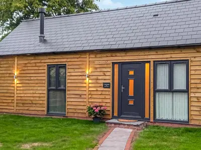 a wooden house with a black door and windows at Cuckoo Lodge - Uk42541 in Winforton