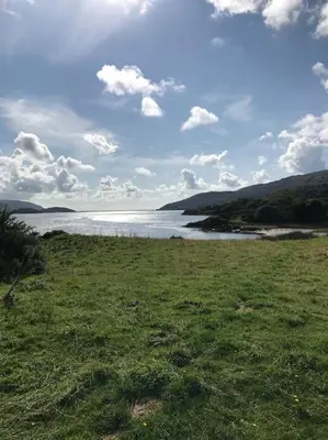 a grassy field with a body of water and clouds at Snowdonia Shepherds Hut + Hot Tub in Barmouth