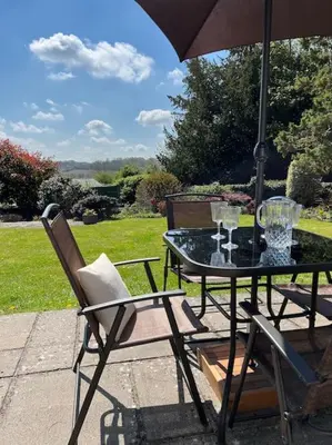 a table and chairs with an umbrella on a patio at A spacious hidden gem with hot tub, lovely garden & views in Kington