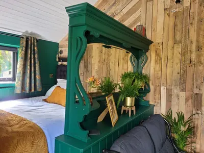 a green bed in a bedroom with wooden walls at Kettle Tree Cabin in Welshpool