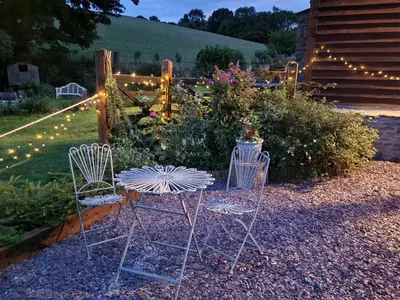 two chairs and a table in a garden with lights at Kettle Tree Cabin in Welshpool