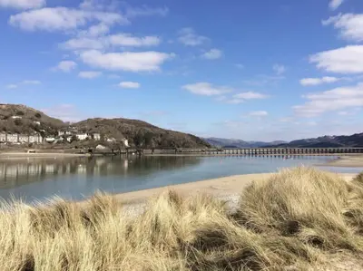 a body of water with a bridge in the background at Lovely cottage in Snowdonia, private hot tub, by mountains & award winning beach in Fairbourne