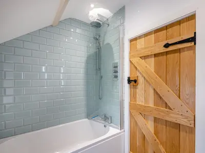 a bathroom with a tub and a shower with a wooden door at Ivy Bush Cottage in Llanddewi-Brefi