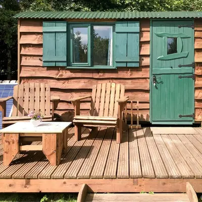 a cabin with two chairs and a table on a deck at Shire the Shepherd's Hut at Pentref Luxury Camping in Penuwch