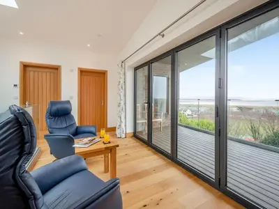 a living room with sliding glass doors with a view of the ocean at Bodwennol - a stunning house! in Aberdyfi