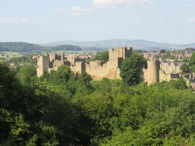 a castle on a hill with trees in the foreground at Llanhedric House in Clun