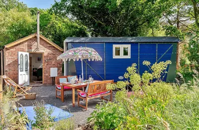 a blue shed with a table and chairs and an umbrella at Finest Retreats - Shrawardine Train Carriage in Shrawardine