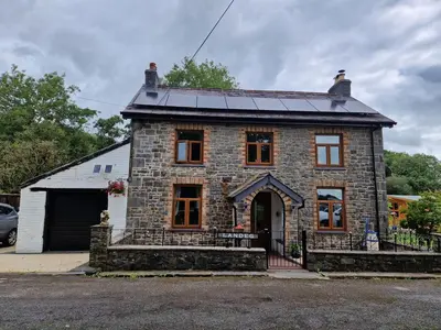 a stone house with a solar roof on a street at Cosy Riverside home in Llanwrda