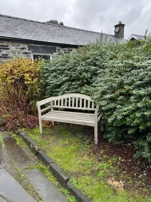 a wooden bench sitting in front of a bush at Robert's Cottage in Abergynolwyn