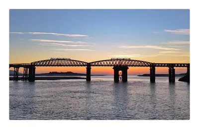 a bridge over the water with a sunset in the background at Robert's Cottage in Abergynolwyn