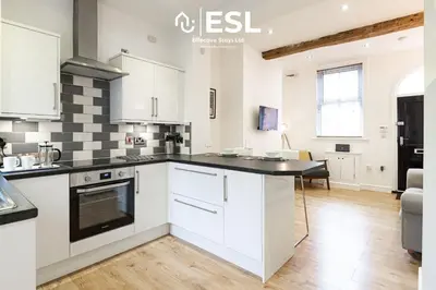 a kitchen with white cabinets and a black counter top at 2 Bedroom Terrace Cottage, Parking, 5 minutes drive to Royal Shrewsbury Hospital in Shrewsbury