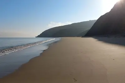 a sandy beach with the ocean and mountains in the background at Gelly Dylan Thomas Paradise in Lampeter
