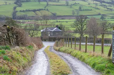 a dirt road leading to a house on a green field at The Barn in Bala