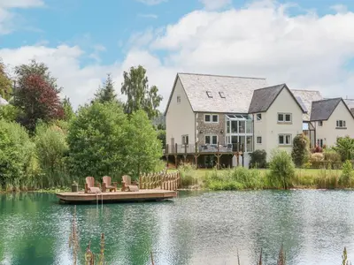 a house on a lake with chairs on a dock at Tan Yr Allt in Welshpool