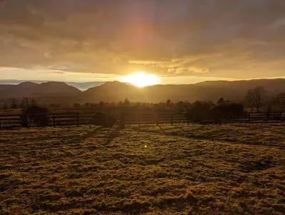 a field with a fence and the sunset in the background at Romantic Hideaway in Trawsfynydd