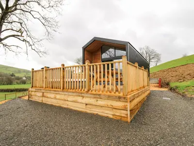 a small house with a wooden deck on a hill at Doe Lodge in Rhayader
