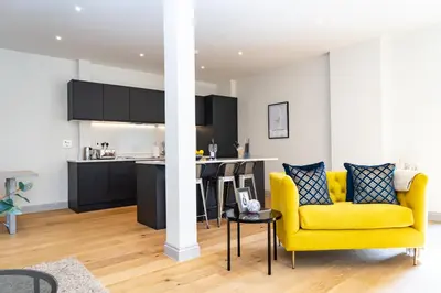 a living room with a yellow couch and a kitchen at The Old Glassworks by Bevolve in Shrewsbury
