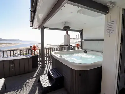 a hot tub on a deck with a view of the ocean at Ty'n-Y-Ffynnon Cottage in Barmouth