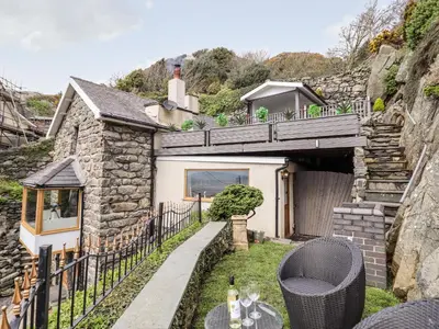a stone house with a bridge over a yard at Ty'n-Y-Ffynnon Cottage in Barmouth