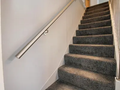 a staircase with grey carpet and a metal hand rail at Wesleyan House in Oswestry