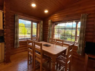 a dining room with a table and chairs and windows at Solid Log Cabin With Private Hot Tub - Oak in Aymestrey