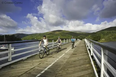 three people riding bikes on a bridge over the water at 2 Bed in Barmouth oc-wah699 in Talybont