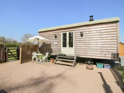 a small house with a table and chairs and an umbrella at Balwen Shepherd's Hut in Montgomery