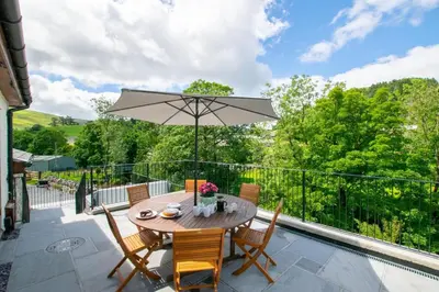 a patio with a wooden table and chairs and an umbrella at 4 Bed in Llanarmon Dyffryn Ceiriog oc-bow151 in Llanarmon Dyffryn-Ceiriog